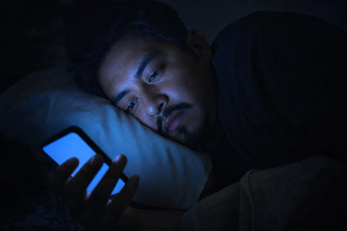 Pantalla de teléfono en la oscuridad con luz azul iluminando la cara de la persona